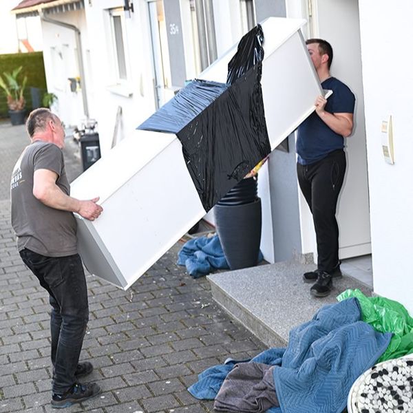 Zwei Umzugshelfer tragen bei einem professionellen Umzug in Ulm einen Schrank aus dem Haus.